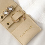 This custom folding jewelry pouch features a snap button and organized interior. It provides an elegant storage solution for jewelry branding.